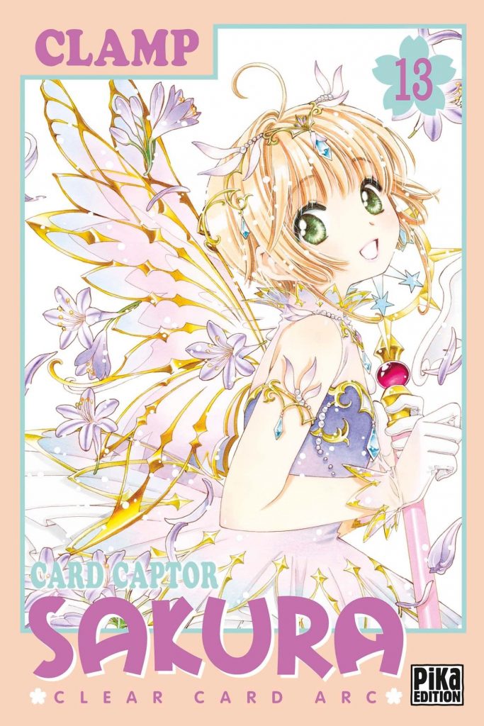 Couverture du tome 13 de Sakura Clear Card. On y voit Sakura de 3/4 dos, avec une robe ornée de dorures. Dans son dos, des ailes façon fée dont le contour est fait de dorure, qui rappellent énormément les ailes dans Trèfle, de CLAMP également. Des lys sont présents un peu partout sur la couverture.